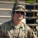 A U.S. Army soldier identified by name tape as 'Watkins' is photographed in a close-up portrait-style image. He is wearing OCP (Operational Camouflage Pattern) uniform with a major's oak leaf insignia, tactical hearing protection headset, sunglasses, and a patrol cap. The setting appears to be an outdoor range or training environment.