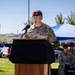 A U.S. Army soldier wearing a maroon beret and multicam uniform is speaking at a wooden podium during an outdoor military ceremony. The name tape on the uniform reads 'STENE' and the soldier wears a U.S. Army branch tape. Several other soldiers in similar uniforms, some also wearing maroon berets, are visible in the background under a blue canopy tent.
