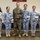 Six military personnel pose for a group photo in front of a wall bearing the word 'SCHOOL' and organizational insignia. Five individuals wear blue digital camouflage uniforms with 'COAST GUARD' patches, consistent with the Philippine Coast Guard, while one individual in the center wears U.S. Marine Corps MARPAT woodland camouflage. All six are holding camouflage covers (patrol caps), suggesting a ceremonial exchange or presentation.