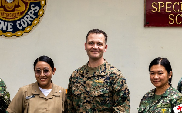 Five military personnel pose for a group photo in front of a 'Specialized School' sign and a Philippine Marine Corps emblem. The group includes members from both the Philippine Marine Corps/Navy and the U.S. Navy/Marine Corps, suggesting a joint military engagement or training event. The setting appears to be inside a Philippine military facility.