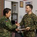 Two military personnel are shaking hands in what appears to be an indoor facility. The individual on the left wears a Philippine Armed Forces uniform with a Philippine flag patch, while the individual on the right wears a U.S. Navy digital camouflage uniform. The U.S. Navy servicemember is holding what appears to be a document or certificate, suggesting a formal exchange or presentation.