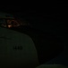 A nighttime photograph of a military aircraft cockpit with a pilot or crew member visible inside. The aircraft fuselage displays the number '1448' and partial lettering 'CE', suggesting a U.S. Air Force designation. The cockpit is dimly illuminated by red instrument lighting, creating a low-light operational atmosphere.