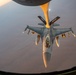 An aerial refueling operation is captured from the perspective of a tanker aircraft, showing an F-16 Fighting Falcon receiving fuel via a boom refueling system. The image is taken during golden hour, casting warm orange light across the aircraft and the arid terrain visible far below. The refueling boom is marked with the number '196' and 'ARW' (Air Refueling Wing) designation.