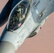 A close-up aerial photograph of an F-16 Fighting Falcon fighter jet in flight, showing the cockpit area with a pilot wearing full flight gear including helmet and oxygen mask. The aircraft bears the tail number '413' and standard military markings including a 'RESCUE' placard near the cockpit. The background suggests the aircraft is flying at altitude over a desert or arid terrain.