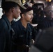The image shows U.S. Navy personnel aboard what appears to be a naval vessel's bridge or combat information center. At least three sailors in dark navy working uniforms and caps are visible, with one centrally positioned sailor wearing a cap marked 'DDG' (destroyer designation). The personnel appear to be monitoring equipment or standing watch at their stations.