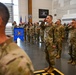 Military personnel in OCP (Operational Camouflage Pattern) uniforms are standing at attention and rendering salutes during a formal ceremony indoors. A blue guidon pennant is visible bearing the markings '194 WG' and '252 COG', indicating this is an Air National Guard unit formation. The ceremony appears to be taking place inside a hangar or large military facility.