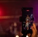 A person is recording a live concert performance on a smartphone mounted in a phone grip/holder. The phone screen displays a guitarist performing on stage, with a recording timer showing 00:07:25. The background shows a dimly lit concert venue with red and purple/magenta stage lighting.