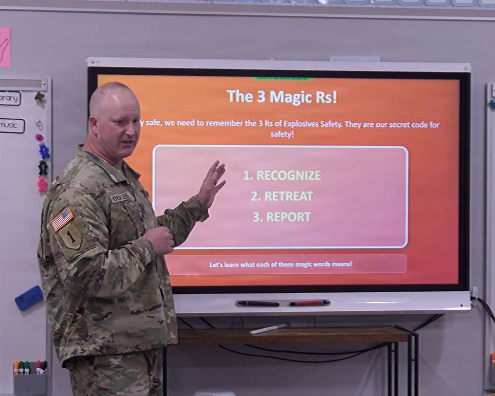 A U.S. Army soldier in OCP camouflage uniform is presenting an explosives safety educational lesson in what appears to be a classroom setting. The presentation slide titled 'The 3 Magic Rs!' outlines three key safety steps: Recognize, Retreat, and Report. The setting and content suggest this is a community outreach or school safety education program.