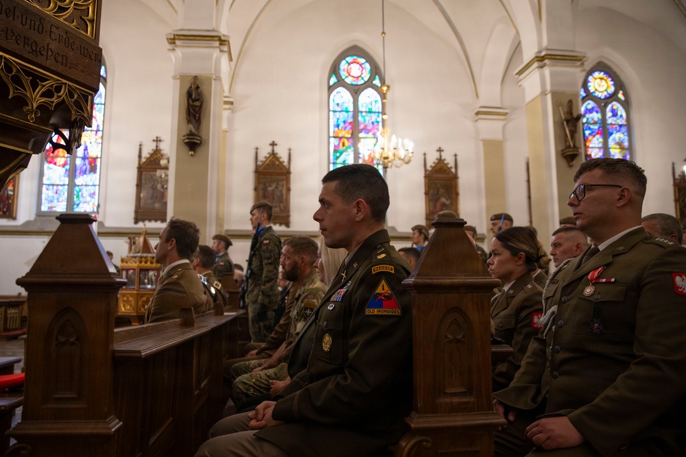 Military personnel from what appears to be both U.S. Army and Polish Army are seated in church pews during a religious ceremony or memorial service. The setting is a Gothic-style Christian church with stained glass windows, vaulted ceilings, and ornate wooden furnishings. The central figure wears U.S. Army dress uniform with visible patches including 'Ranger' and 'Old Ironsides' (1st Armored Division).