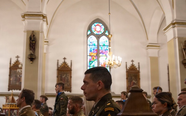 Military personnel from what appears to be both U.S. Army and Polish Army are seated in church pews during a religious ceremony or memorial service. The setting is a Gothic-style Christian church with stained glass windows, vaulted ceilings, and ornate wooden furnishings. The central figure wears U.S. Army dress uniform with visible patches including 'Ranger' and 'Old Ironsides' (1st Armored Division).