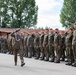 A military parade or inspection ceremony is taking place outdoors on a paved surface. Two senior officers in dress uniforms are walking and saluting while reviewing a formation of soldiers standing at attention in camouflage uniforms. The soldiers display Polish flag patches on their shoulders, indicating this is a Polish Armed Forces event.