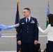 A U.S. Air Force service member in dress blues is having insignia or rank devices pinned onto his shoulders by two young people, likely family members, during a formal military promotion ceremony. The setting appears to be an official indoor venue with Air Force flags visible in the background. This type of ceremony traditionally involves family members placing new rank insignia on the service member.
