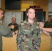 A U.S. Air Force military ceremony appears to be taking place in what looks like an operations center or command room. A service member named 'Steadman' (visible on name tape) is standing at attention while two other personnel appear to be conducting a coin or tapping ceremony on both sides. Several other military personnel are observing in the background.