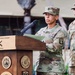 A U.S. Army soldier with the name tape 'HARRIS' and Sergeant Major rank insignia is speaking at a podium during an official military ceremony for the 94th Army Air &amp; Missile Defense Command. A second U.S. Army soldier stands at attention in the background. The podium bears the inscription 'First Line of Defense' along with multiple military unit emblems.