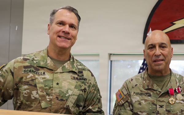 Two U.S. Army soldiers in MultiCam/OCP camouflage uniforms are posing together while holding a ceremonial saber mounted on a wooden display plaque. The soldier on the left is identified by name tape as 'SCARCELLA' and wears a Brigadier General star insignia, while the soldier on the right is identified as 'FARABAUGH' and wears a Colonel eagle insignia along with multiple medals including what appears to be a Meritorious Service Medal. This appears to be a military retirement or award ceremony presentation.