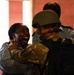 The image shows a tense interaction between a civilian woman and a soldier wearing military camouflage and a combat helmet. The woman appears distressed and is shouting, while the soldier appears to be restraining or guiding her. Additional individuals in blue uniforms, possibly police officers, are visible in the background.