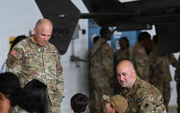 The image shows a military gathering inside what appears to be an aircraft hangar, with U.S. Army soldiers in OCP (Operational Camouflage Pattern) uniforms interacting with civilians including children. A senior officer identified by the name tape 'BLANCHARD' and a general officer star is visible speaking with a soldier who is engaging with two young boys. The setting suggests a family day, unit ceremony, or pre/post-deployment event.