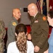A military ceremony or reception is taking place in a formal indoor setting with flags displayed in the background. Two senior military officers are shaking hands at the center of the image, while other personnel and civilians look on. The setting appears to be an official military function, possibly a promotion, retirement, or change of command ceremony.