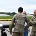 Three individuals are gathered on a military flight line or tarmac near an aircraft. Two are wearing U.S. Army OCP (Operational Camouflage Pattern) uniforms, while one civilian woman in casual attire stands between them. The senior uniformed individual on the right displays a name tape reading 'BLANCHARD' and appears to hold a general officer rank based on visible insignia.