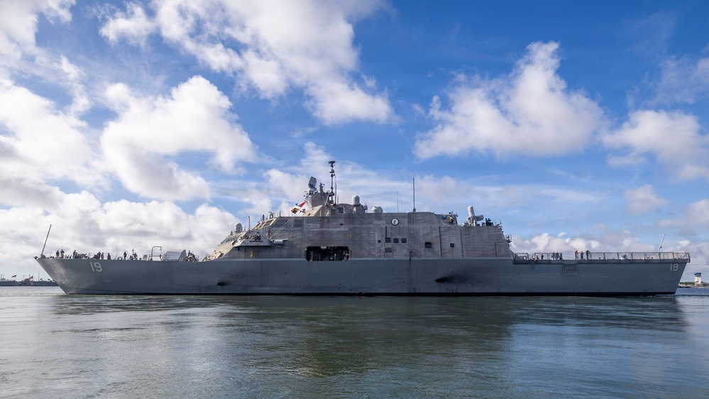 A U.S. Navy Littoral Combat Ship bearing hull number 19 is photographed underway or maneuvering in calm harbor waters. The vessel displays the characteristic flat, angular design of the Freedom-class LCS with a low freeboard and prominent superstructure. Personnel are visible on deck, suggesting the ship is in an active operational status.