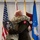 Col. Finch Concludes Distinguished Career, Leaves Lasting Legacy as Command State Chaplain Two military personnel in uniform are embracing during what appears to be a formal military ceremony. One individual is wearing Army Combat Uniform (ACU/OCP) with a unit patch visible on the sleeve, while the other is in a dark military jacket. A commemorative medallion or plaque is visible being held during the embrace.