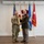 Col. Finch Concludes Distinguished Career, Leaves Lasting Legacy as Command State Chaplain Two military personnel are posing together while jointly holding a large brass artillery shell casing, likely during a formal military ceremony or award presentation. One individual is wearing Army Combat Uniform (ACU/OCP pattern) and the other is in Army Service Uniform (green dress uniform) with multiple medals and insignia. Several flags are displayed in the background, including the U.S. flag, Florida state flag, Air Force flag, and a general officer flag with one star.