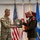 Col. Finch Concludes Distinguished Career, Leaves Lasting Legacy as Command State Chaplain Two military officers are participating in a formal award or recognition ceremony, with one presenting a commemorative plaque to the other. The plaque bears the name 'Glenn H. Finch' and the title 'Chaplain (Colonel)'. The ceremony takes place in front of multiple military flags representing various branches of the U.S. Armed Forces.