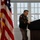 Col. Finch Concludes Distinguished Career, Leaves Lasting Legacy as Command State Chaplain A U.S. Army officer in dress uniform stands at a dark podium, appearing to review notes or prepare to speak. The setting appears to be an official military ceremony or briefing held indoors. An American flag is prominently displayed to the left of the frame.