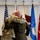 Col. Finch Concludes Distinguished Career, Leaves Lasting Legacy as Command State Chaplain Two military personnel in uniform are embracing in what appears to be an official ceremony. They are standing in front of a display of military flags including the U.S. flag, an Air Force flag, and a general officer flag. The setting suggests a formal military event such as a change of command, retirement, or promotion ceremony.