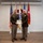 Col. Finch Concludes Distinguished Career, Leaves Lasting Legacy as Command State Chaplain Two U.S. Army officers in service dress uniforms are posing together while jointly holding a certificate or award document. The setting appears to be a formal military ceremony room with multiple flags displayed in the background. This appears to be an awards or recognition ceremony.