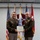 Col. Finch Concludes Distinguished Career, Leaves Lasting Legacy as Command State Chaplain Two U.S. Army officers in dress green uniforms are jointly holding a certificate during a formal military award ceremony. The certificate appears to be 'The Florida Cross' awarded for 'Exceptionally Meritorious Service' to a Colonel. The ceremony is taking place indoors with multiple military flags displayed in the background.