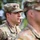 The image shows multiple U.S. Army soldiers in Operational Camouflage Pattern (OCP) uniforms standing in formation. The central figure, identified by a name tape as 'PRUITT,' is in sharp focus and appears to be at attention or participating in a formal military ceremony or formation. An American flag patch is visible on the left shoulder of the central soldier.