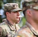 The image shows multiple U.S. Army soldiers in Operational Camouflage Pattern (OCP) uniforms standing in formation. The central figure, identified by a name tape as 'PRUITT,' is in sharp focus and appears to be at attention or participating in a formal military ceremony or formation. An American flag patch is visible on the left shoulder of the central soldier.