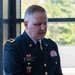 A U.S. Army soldier in dress blues uniform is photographed indoors near a large window with trees visible in the background. The soldier's name tape reads 'GAGNON' and displays multiple service ribbons and insignia. He appears to be looking downward, possibly reading or speaking at a formal event.