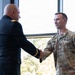 Two U.S. Army personnel are shaking hands in what appears to be an official or ceremonial setting. One individual is wearing a formal Army Service Uniform (ASU) in dark blue, while the other is wearing Operational Camouflage Pattern (OCP) combat uniform with the name tape 'BERGERON' and U.S. Army tape visible. The setting appears to be an indoor facility with large windows in the background.