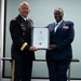 Two military officers are posing together while jointly holding a framed Certificate of Retirement from the United States Air Force. The officer on the left wears a U.S. Army dress uniform with the name tag 'BERRY,' while the officer on the right wears a U.S. Air Force dress uniform adorned with multiple medals and ribbons. The ceremony appears to be an official military retirement presentation.