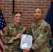 Two U.S. Air Force personnel are posing together holding a Certificate of Promotion to the rank of Airman First Class for 'Randell M. Luterte.' The ceremony appears to take place in front of an American flag and what appears to be the Maine state flag (featuring the word 'Dirigo'). Both individuals are wearing OCP (Operational Camouflage Pattern) uniforms.