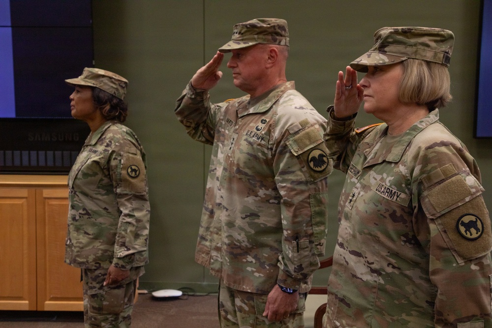 Three U.S. Army soldiers in Operational Camouflage Pattern (OCP) uniforms are standing at attention during a formal military ceremony. Two of the three individuals — the center male soldier and the right female soldier — are rendering a salute, while the left female soldier stands at attention. All three wear shoulder patches consistent with the same unit, visible on their left sleeves.