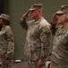 Three U.S. Army soldiers in Operational Camouflage Pattern (OCP) uniforms are standing at attention during a formal military ceremony. Two of the three individuals — the center male soldier and the right female soldier — are rendering a salute, while the left female soldier stands at attention. All three wear shoulder patches consistent with the same unit, visible on their left sleeves.
