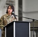 A U.S. Air Force service member stands at a black podium with a microphone, appearing to speak or prepare to speak at a formal military ceremony or event. The individual is wearing an OCP (Operational Camouflage Pattern) uniform with a name tape reading 'RUSSO' and a 'U.S. AIR FORCE' tape visible. The setting appears to be inside a large military hangar or similar facility.