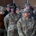 A group of U.S. Army soldiers and what appears to be at least one German Bundeswehr soldier are assembled in what looks like a military hangar or large indoor facility. Two U.S. Army soldiers are prominently visible in the foreground — one named BRAHAM wearing a distinctive cavalry Stetson hat with sergeant chevrons, and another named OLMEDO. The gathering appears to be a formal military formation or briefing event.