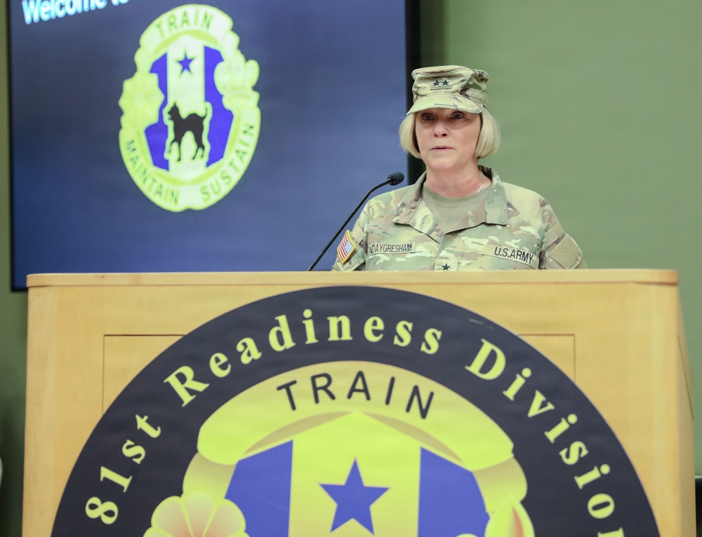 A U.S. Army Major General is speaking at a podium for the 81st Readiness Division. The officer, identified by the name tape as 'DAYGRESHAM' and wearing two-star rank insignia, is dressed in Army Combat Uniform (ACU) with OCP (Operational Camouflage Pattern). The setting appears to be an official military briefing or ceremony.