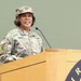 A U.S. Army Major General named Wallace is speaking at a podium during an official military event. She is wearing the Army Combat Uniform (ACU) in Operational Camouflage Pattern (OCP) with two-star rank insignia visible on both her cap and chest. The setting appears to be an indoor military ceremony or briefing.