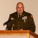 A U.S. Army officer identified by nameplate as 'ETLING' is speaking at a wooden podium with a microphone. He is wearing the Army Green Service Uniform adorned with multiple rows of service ribbons, badges, and insignia. The setting appears to be a formal military ceremony or official function.