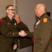 Two U.S. Army officers in Army Service Uniforms (green dress uniforms) are shaking hands at what appears to be a formal military ceremony or event. The officer on the left, identified by his name tape as 'KRZAN,' is smiling and wearing glasses, while the officer on the right displays a Pennsylvania National Guard shoulder patch. Additional military personnel are visible in the background.