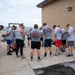 A group of approximately 12-15 individuals wearing matching gray 'Crash Rescue' t-shirts are gathered in a circle with heads bowed, appearing to be in prayer or a moment of reflection. The shirts reference '186th ARW - Key Field' and 'Crash Rescue,' indicating these are Air National Guard crash rescue personnel. The gathering takes place on a concrete pad adjacent to a brick building, likely at Key Field Air National Guard Base in Mississippi.