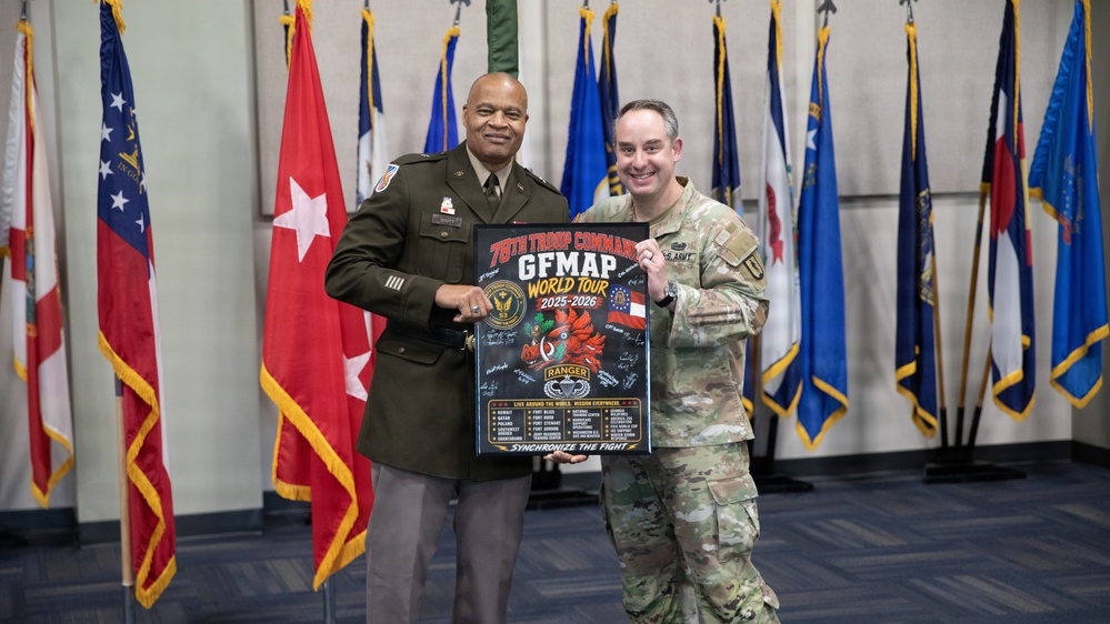 Two U.S. Army personnel are posing together while holding a framed poster reading '78th Troop Command GFMAP World Tour 2025-2026' with the tagline 'Synchronize the Fight.' The setting appears to be an official military ceremony room with multiple state and military flags displayed in the background. One individual is in Army Service Uniform (green) and the other is in Army Combat Uniform (OCP/multicam).