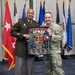 Two U.S. Army personnel are posing together while holding a framed poster reading '78th Troop Command GFMAP World Tour 2025-2026' with the tagline 'Synchronize the Fight.' The setting appears to be an official military ceremony room with multiple state and military flags displayed in the background. One individual is in Army Service Uniform (green) and the other is in Army Combat Uniform (OCP/multicam).