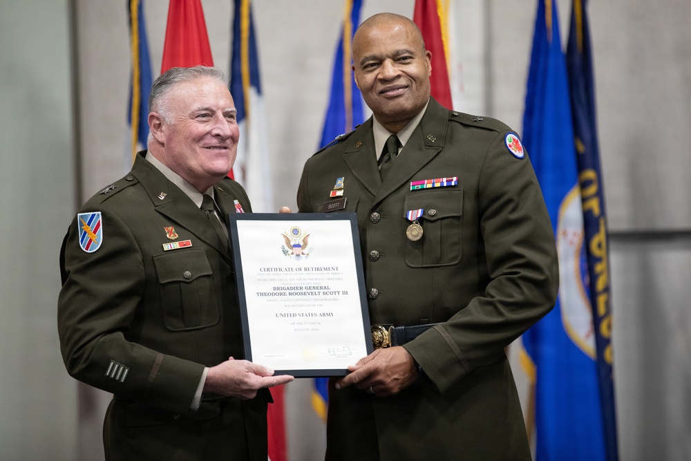 Two U.S. Army officers in olive green dress uniforms are posing together while holding a Certificate of Retirement. The certificate is issued to Brigadier General Theodore Roosevelt Scott III upon his retirement from the United States Army. The ceremony appears to be a formal military retirement event with flags displayed in the background.