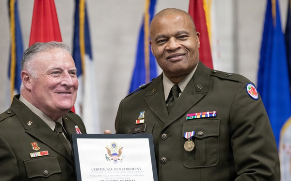 Two U.S. Army officers in olive green dress uniforms are posing together while holding a Certificate of Retirement. The certificate is issued to Brigadier General Theodore Roosevelt Scott III upon his retirement from the United States Army. The ceremony appears to be a formal military retirement event with flags displayed in the background.
